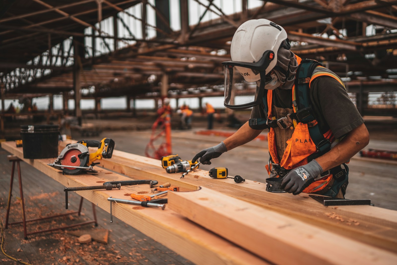 man in orange and black vest wearing white helmet holding yellow and black power tool worker' compensation
